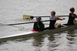 Team rowing in a race, coxswain guiding while athletes row on a river, boat with number 166.