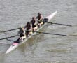 Four women rowing a boat in sync on a calm river during a sunny day.
