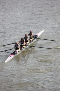 Four women rowing a boat in sync on a calm river during a sunny day.
