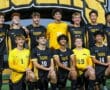 Soccer team posing in black and yellow uniforms with Tigers logo, group photo on the field.