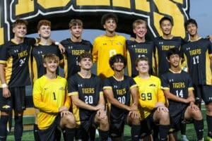 Soccer team posing in black and yellow uniforms with Tigers logo, group photo on the field.