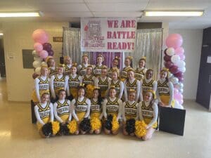 Cheerleading team in yellow uniforms poses at Battle at the Bridge event, ready for performance.