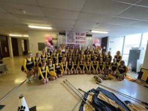 Cheerleading team in yellow uniforms posing indoors with balloons and decorations.