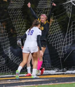 Soccer player celebrates a goal, opponent reacts in front of net; intense game moment capturing victory and defeat.