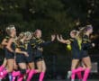 Soccer team in black and pink celebrates a goal, players high-fiving joyfully on the field at night.