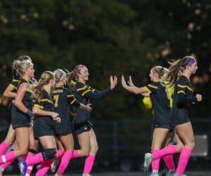 Soccer team in black and pink celebrates a goal, players high-fiving joyfully on the field at night.