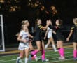 High school girls' soccer match; players celebrate on the field under stadium lights.