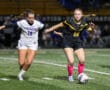 Two female soccer players in action on the field at night, focused on the ball.