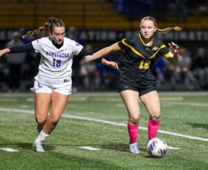 Two female soccer players in action on the field at night, focused on the ball.