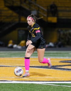 Soccer player dribbling ball on field, wearing pink socks and headband, focused on the game.