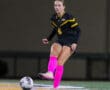 Soccer player in black and yellow uniform, pink socks, kicking ball on field at night.