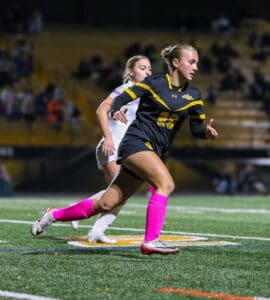 Soccer player in black uniform with pink socks sprinting during a match at night.