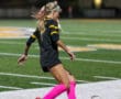 Female soccer player in black and yellow uniform kicking ball on field at night.