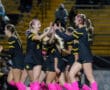 Girls' soccer team celebrates with high-fives, wearing black uniforms with pink socks on the field at night.