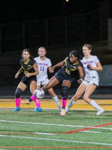 Soccer players competing for the ball during a night match on a field with colorful socks and determined expressions.