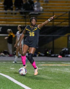 Soccer player in black jersey with pink socks directing teammates on field during night match.