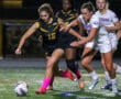 Female soccer players competing intensely on field during night game.