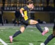Soccer player in black and yellow uniform sprinting on field during night match, focused on ball control.