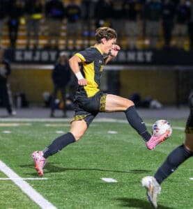 Soccer player in black and yellow uniform sprinting on field during night match, focused on ball control.
