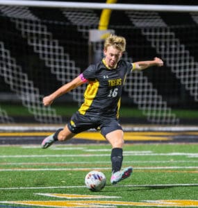 Soccer player in black and yellow uniform kicks ball on field at night.