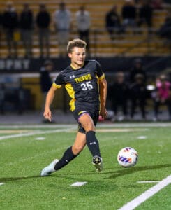 Soccer player in black jersey kicking ball on field during match at night.