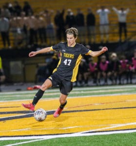 Soccer player in action, wearing Tigers jersey #47, controls the ball mid-air during a night match.