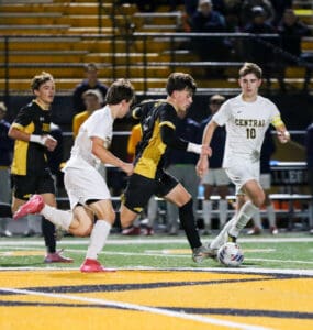 Soccer players compete intensely on the field in a nighttime match, wearing black and white team uniforms.