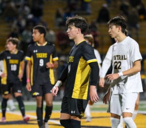 High school soccer players from rival teams during a night match. Players in focus wearing black and white jerseys.