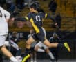 Soccer player in black and yellow jersey running with ball during night game.