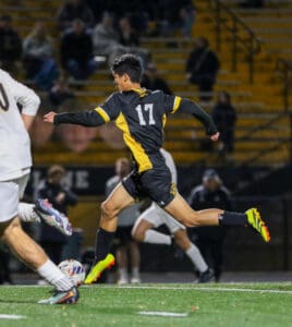 Soccer player in black and yellow jersey running with ball during night game.