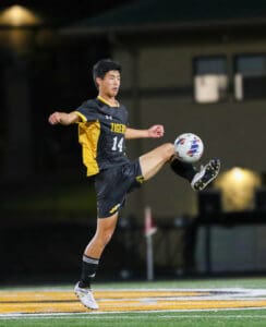 Soccer player in black and yellow uniform kicking a ball during a night game on the field.