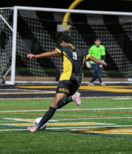 Soccer player in yellow and black uniform taking a shot at goal during a night match.