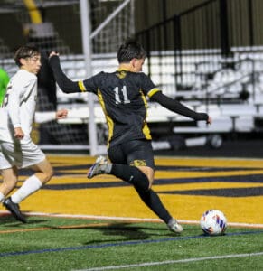 Soccer player in black and yellow jersey kicks ball towards goal on a colorful field during a match.