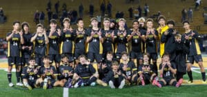 Youth soccer team celebrating victory on the field, wearing black and yellow uniforms.