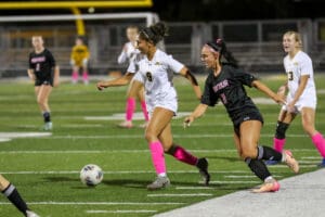 Girls' soccer match in action, players from opposing teams competing for the ball on the field.