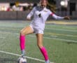 Soccer player in action on field during a night match, wearing pink socks and white jersey.