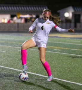 Soccer player in action on field during a night match, wearing pink socks and white jersey.