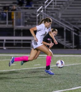 Soccer players in action during a night game, wearing white and pink gear, competing for the ball on the field.