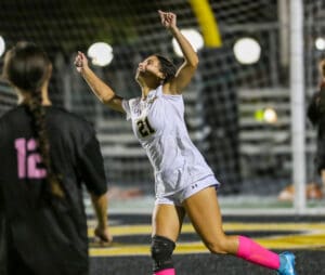 Soccer player in white jersey celebrating a goal on the field at night.