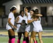 Soccer players in pink socks celebrate on the field after a match under stadium lights.