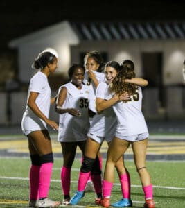 Soccer players in pink socks celebrate on the field after a match under stadium lights.
