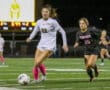 Two soccer players compete on a field under bright stadium lights, focused on controlling the ball.