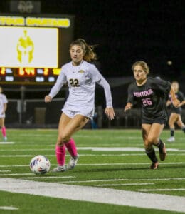 Two soccer players compete on a field under bright stadium lights, focused on controlling the ball.