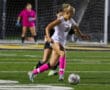 Soccer player in white dribbles past defender on a field at night, wearing bright pink socks.