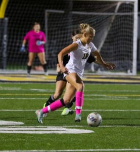 Soccer player in white dribbles past defender on a field at night, wearing bright pink socks.