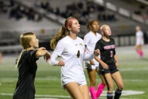 Girls soccer match in progress under stadium lights, players focused on the ball, competing on the field.