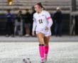 Soccer player in white kit and pink socks and headband with ball on the field at night game.