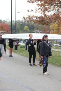 Rowing team carrying a boat on a pathway with autumn trees in the background.