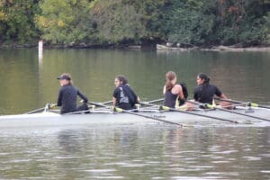 Rowing team practices on calm river, surrounded by lush trees, under a clear sky.