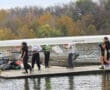 Rowing team carrying boat on dock by a lake during autumn.